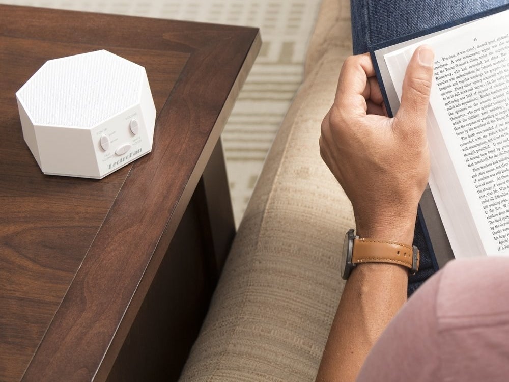 The white noise machine sitting on a side table while Model reads a book