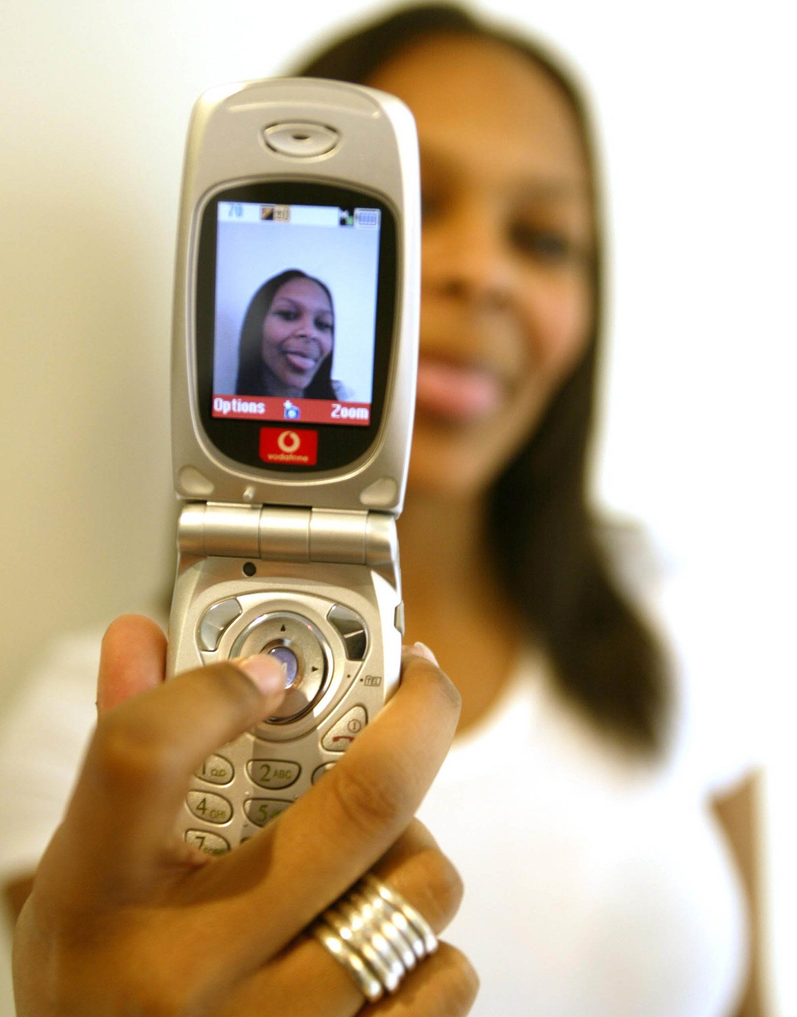 A Samantha holding the flip phone screen towards the camera and her face (her sticking out her tongue) is in the center of the screen.