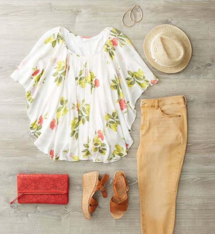 Flatlay of a floral top, tan denim pants, wedge sandals, straw hat, gold hoop earrings, and a  small red purse. 