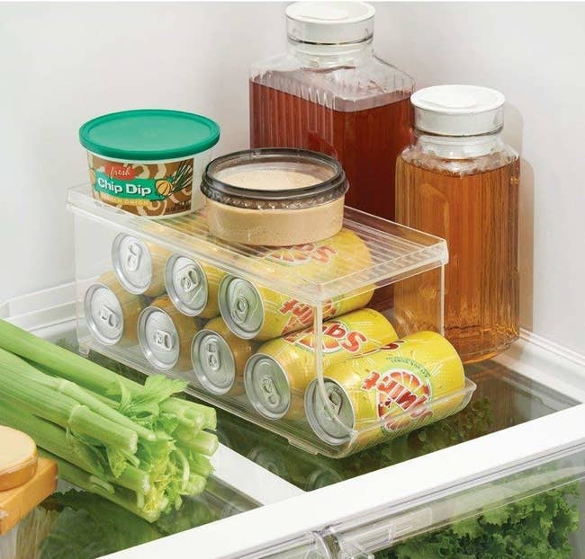 clear acrylic holder in fridge with eight soda cans on their side in two layers; a closed top acts as a shelf for other groceries
