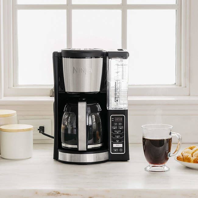 A lifestyle shot of the coffee maker in a kitchen with a hot cup of coffee