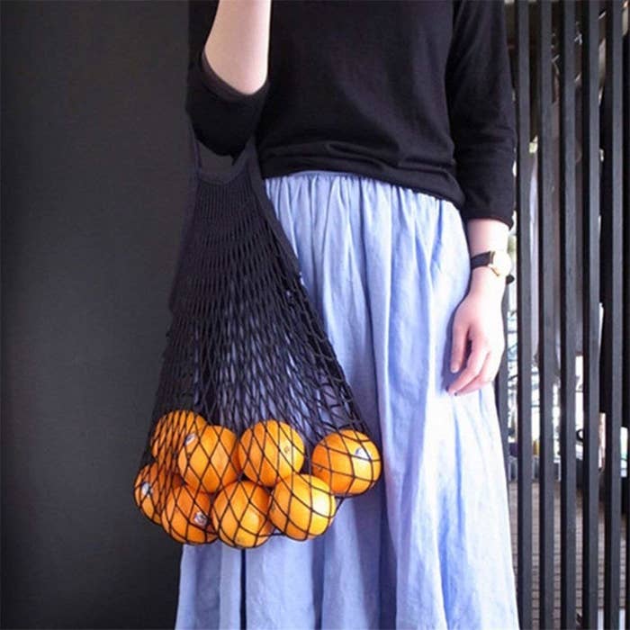 A person holding the net grocery bag filled with oranges