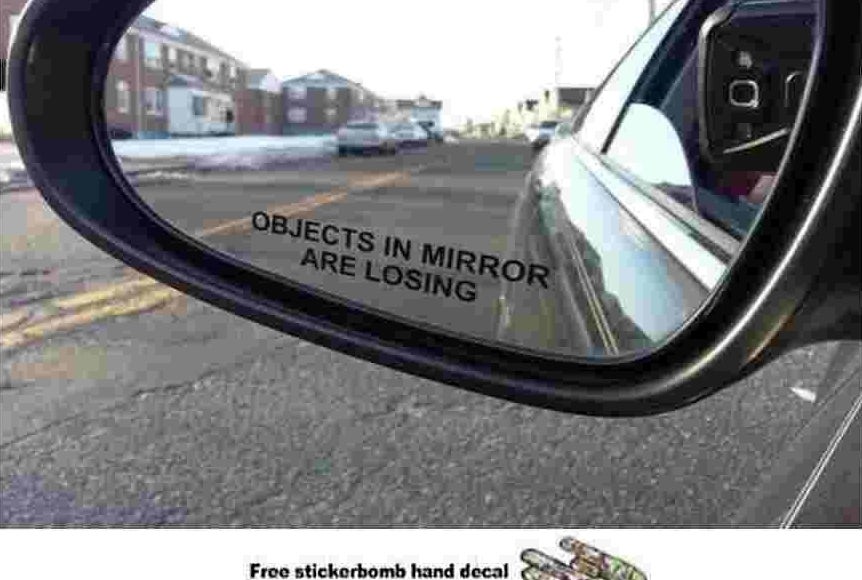 A close up of a car&#x27;s side mirror with the sticker, &quot;objects in mirror are losing&quot;
