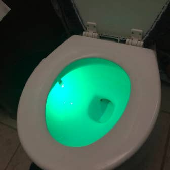 A different reviewer image showing their toilet seat shining bright green in a room with the lights turned on