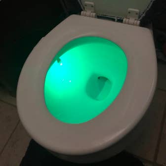 A different reviewer image showing their toilet seat shining bright green in a room with the lights turned on