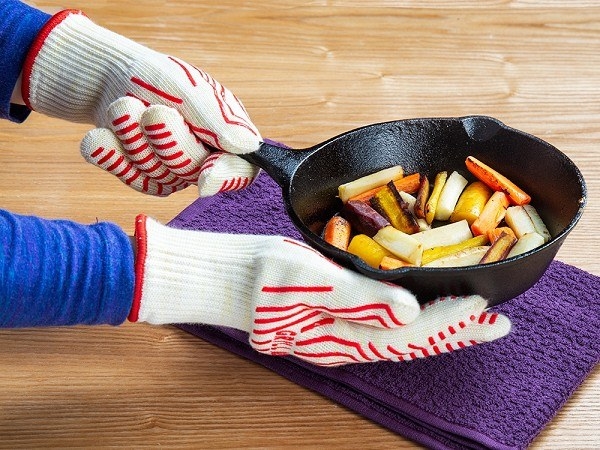 Hands with heat resistant gloves on directly holding skillet with veggies