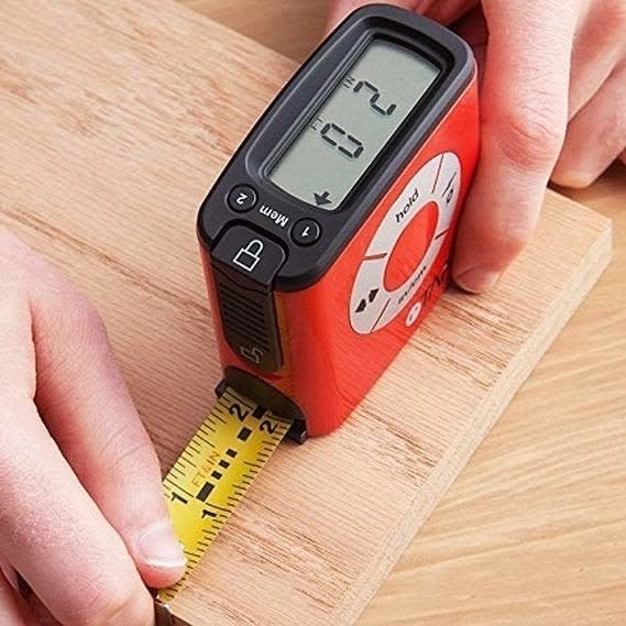 Hands holding and using the digital measuring tape, with the screen displaying the exact measurements