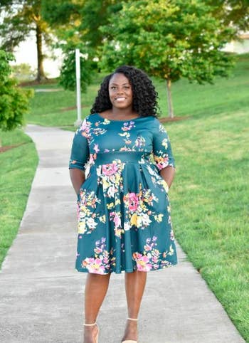 Reviewer wearing the boat neck 3/4-sleeve dress in teal with pink and green flowers all over it