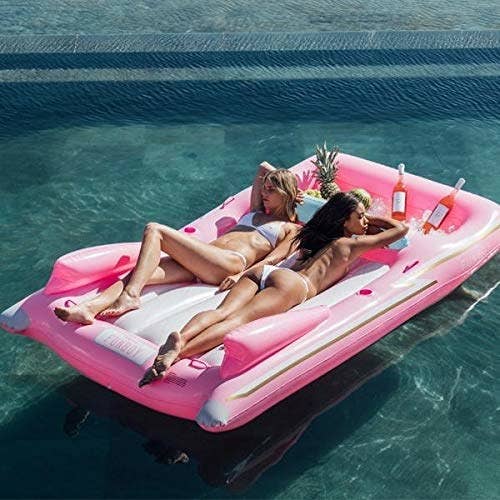 Two models lounging on the pink pool float