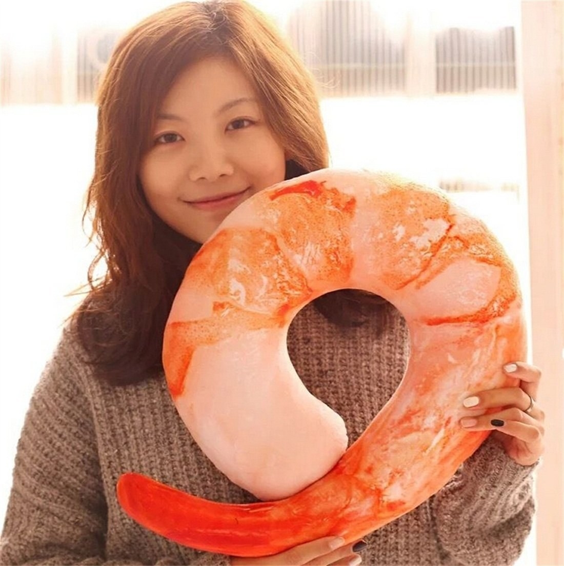 person holding the neck pillow that looks like a shrimp