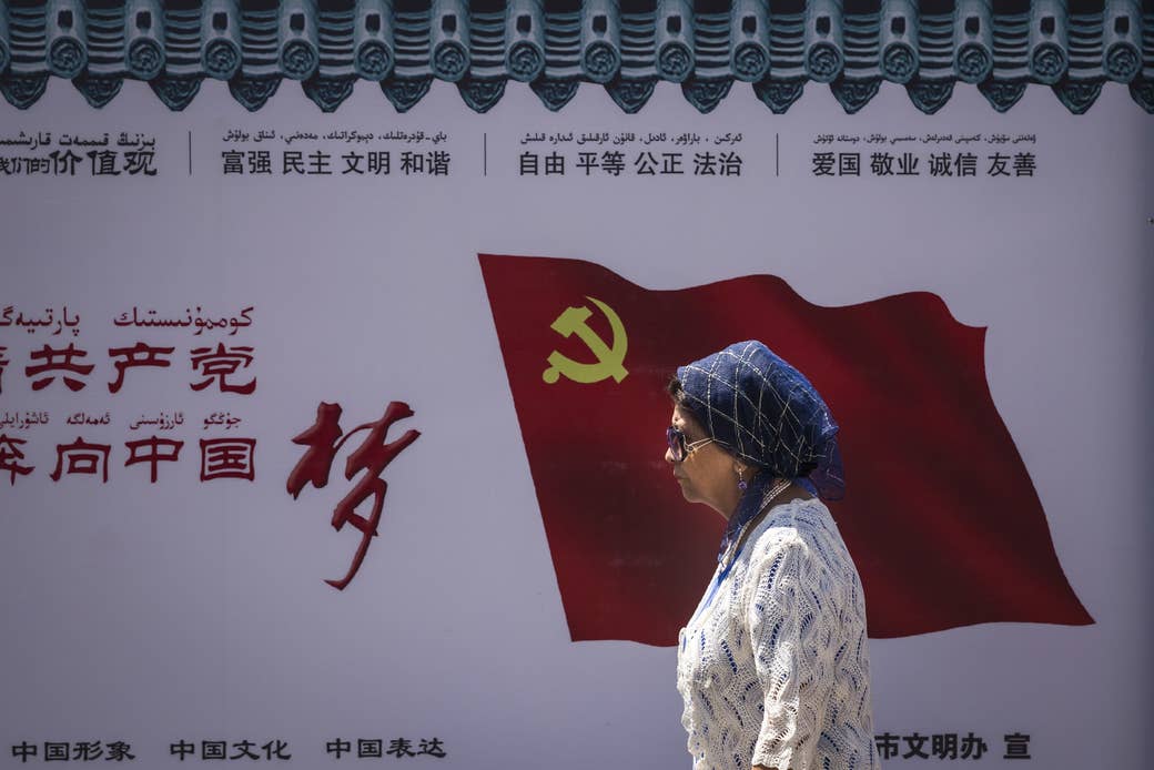 A Uighur woman passes the Communist Party of China flag on the wall on June 27, 2017, in Ürümqi, China.