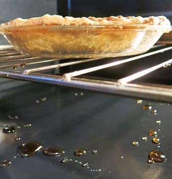 An oven liner catching the remnants of a pie baking inside the oven