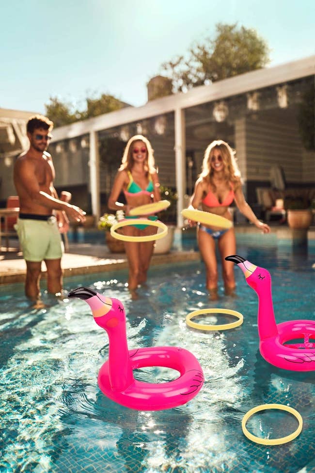 Three models playing ring toss with the flamingos while standing inside a pool