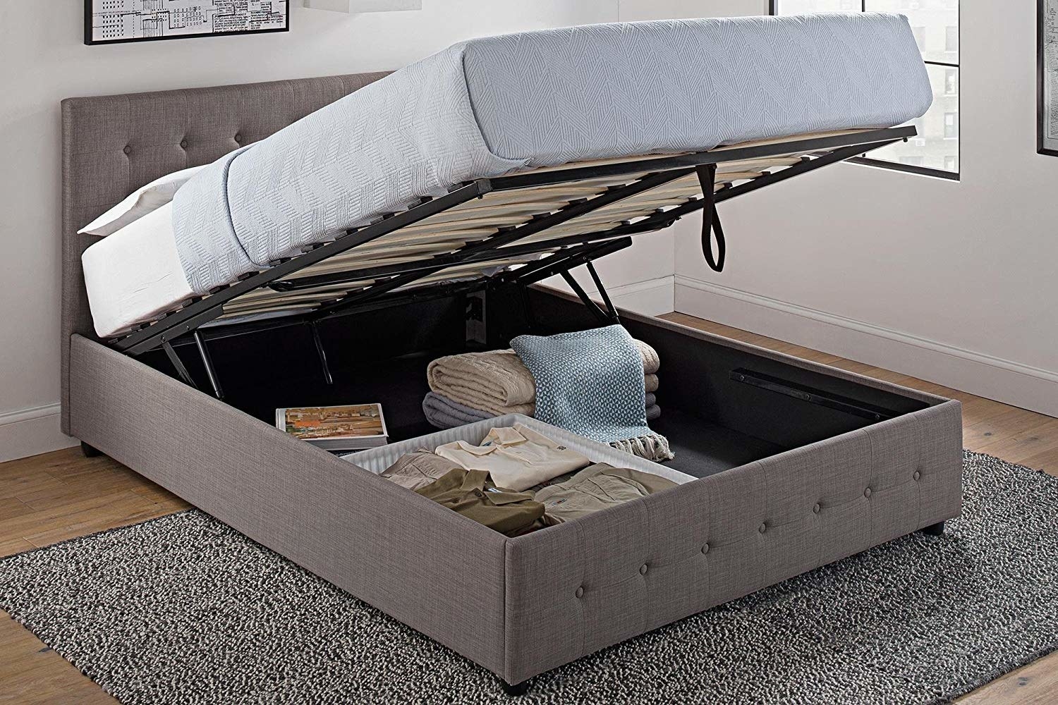 The bed, with the mattress lifted and blankets, storage bins with clothing showing in the storage space