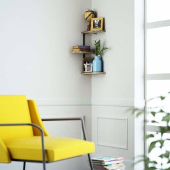 the three-tier corner bookshelf on a wall above a yellow armchair