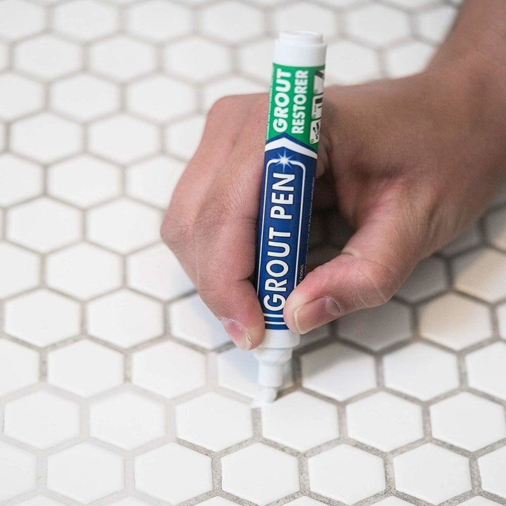 someone coloring in dirty grout with the grout pen, making it white again