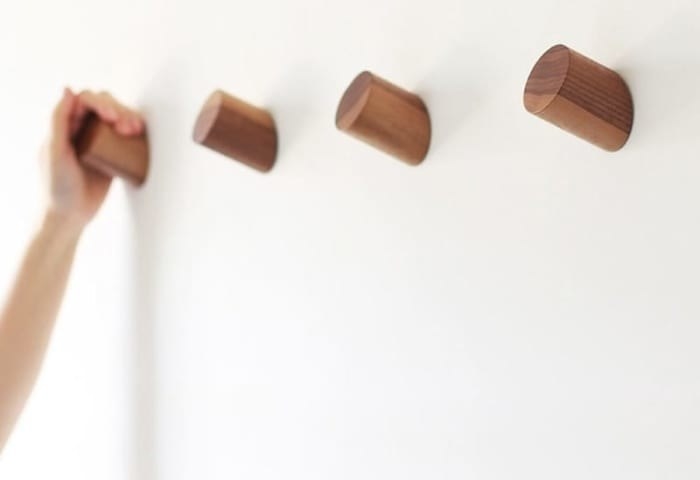 Four simple wood wall hooks with a hand on the farthest one away