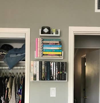 Floating shelves on a wall in between two doorways with the bottom two filled with books and the top with a candle