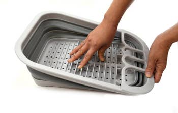 a pair of hands holding the collapsible dish rack