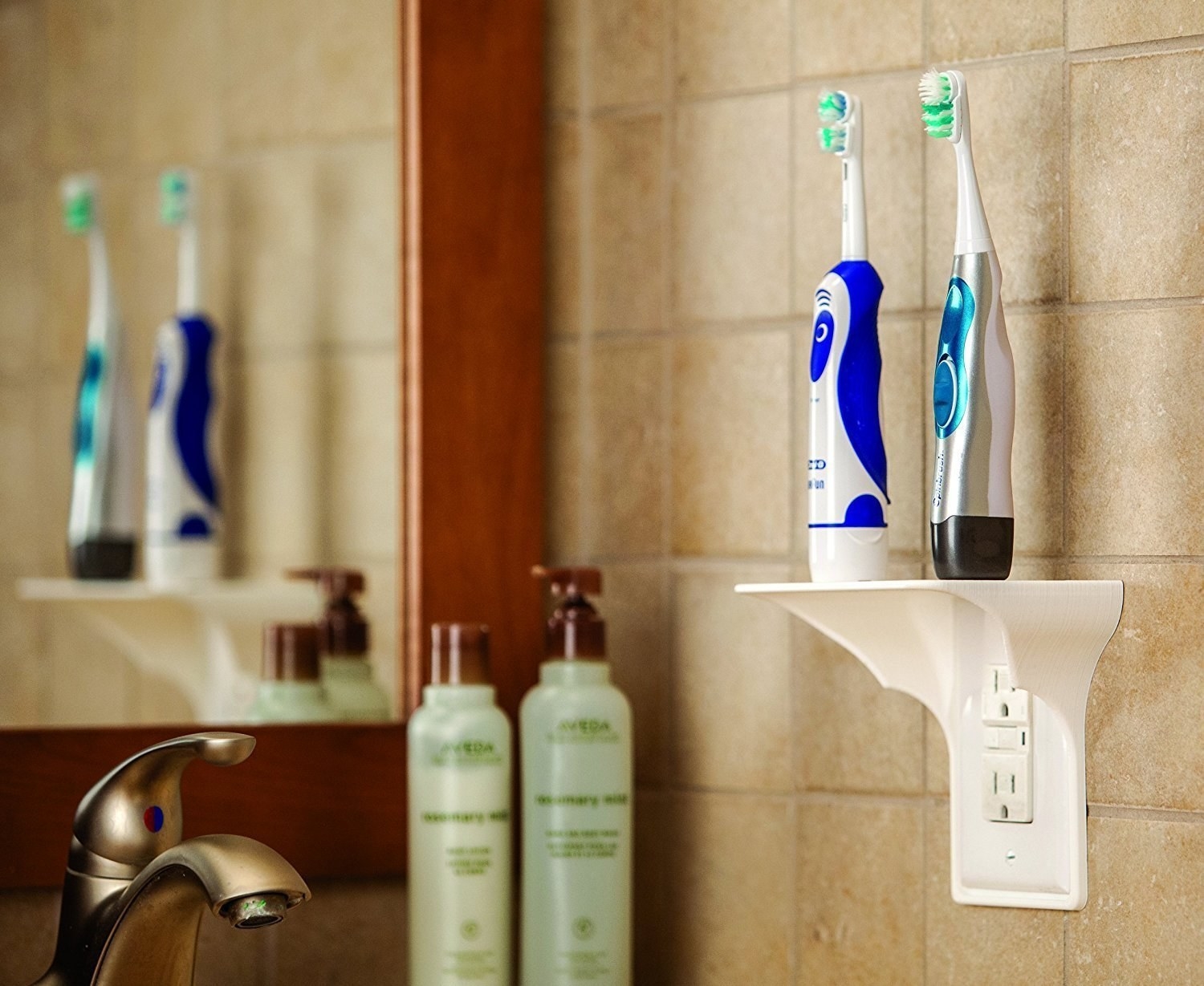 Two electric toothbrushes sitting on a small shelf above an outlet in a bathroom 