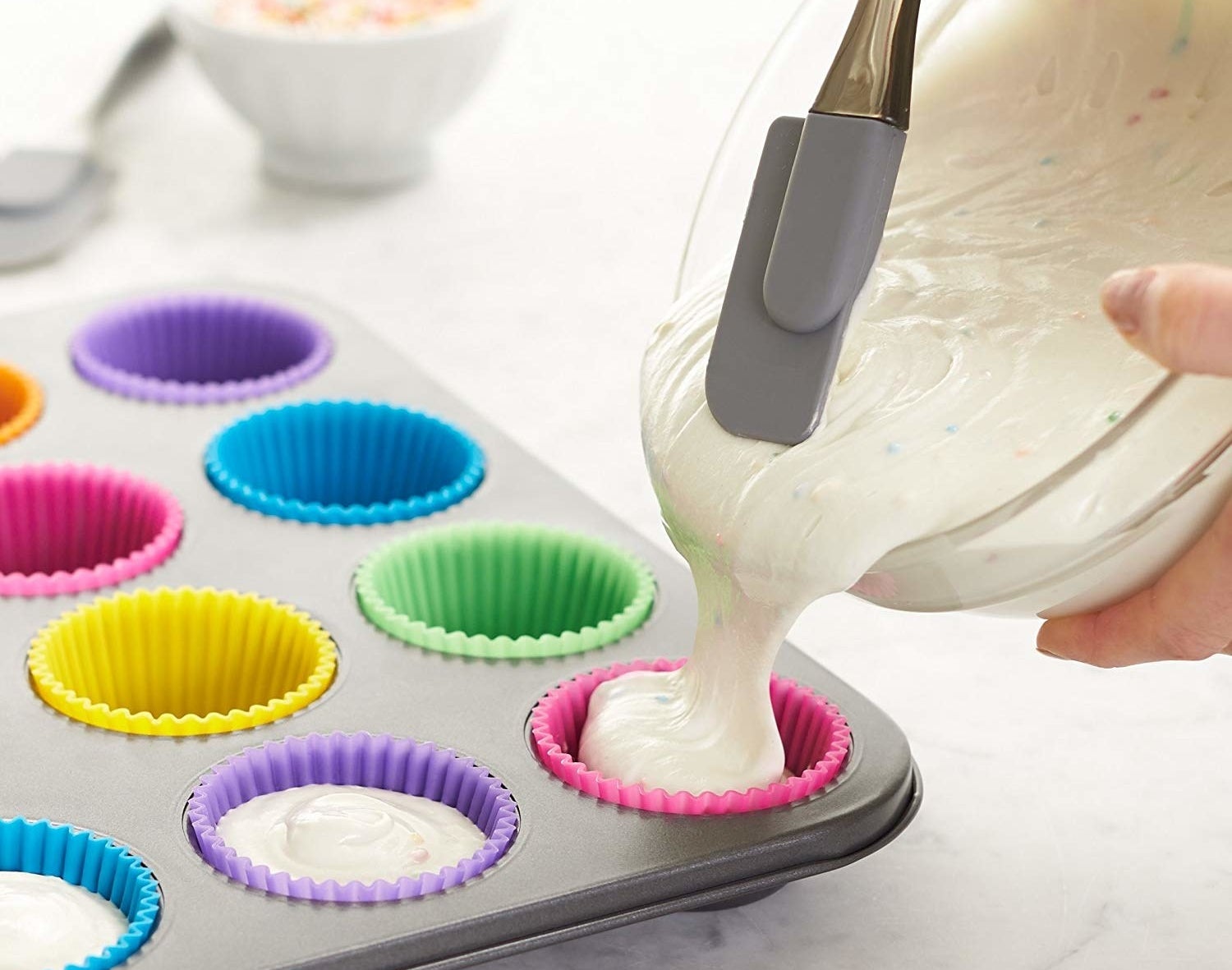 A person pouring batter into the reusable silicone baking cups