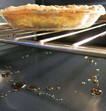 A non-stick oven liner at the bottom of an oven with sticky pie remnants on it