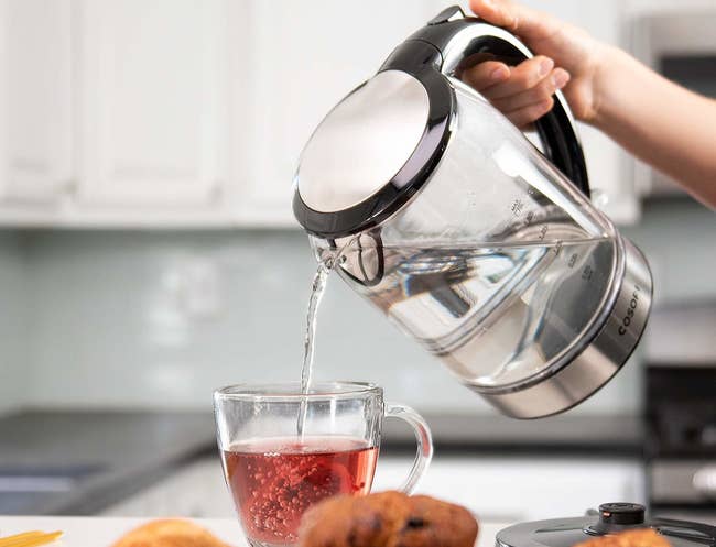 A person pouring boiling water from the kettle into a mug of tea