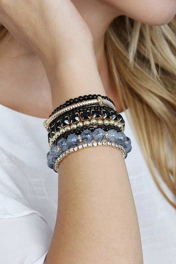 A model wearing a stack of black, gray, and gold bracelets in different materials and thicknesses