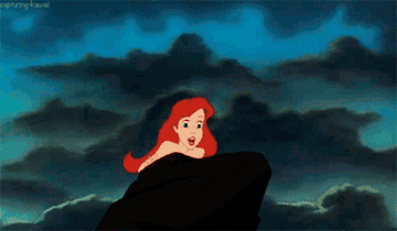 ariel from the little mermaid pushing herself on a rock as water splashes behind her