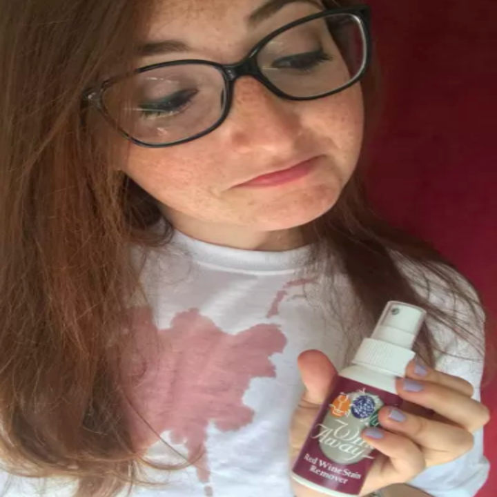 BuzzFeed writer holding bottle of red wine stain remover with stain on their white t shirt 