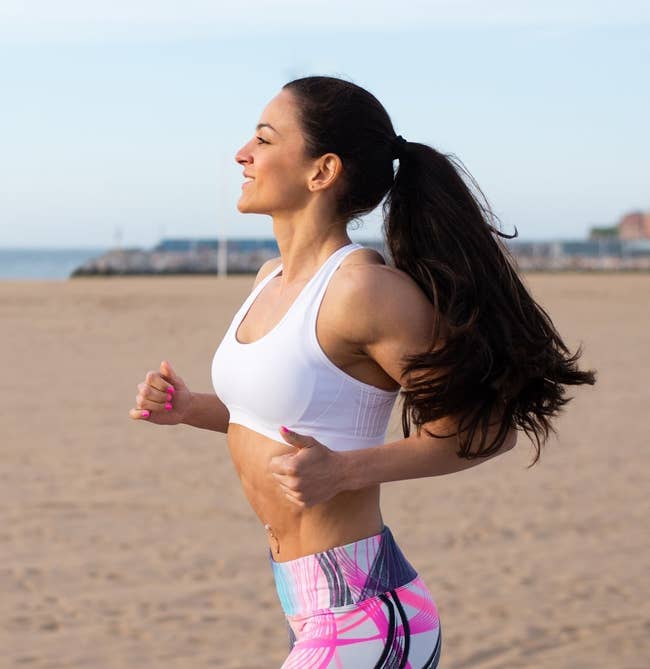 model with thick hair in a ponytail jogging on a beach