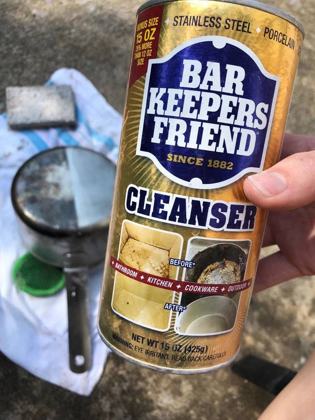 the can of cleanser held by reviewer in front of pan that is half cleaned to show how effective it is 
