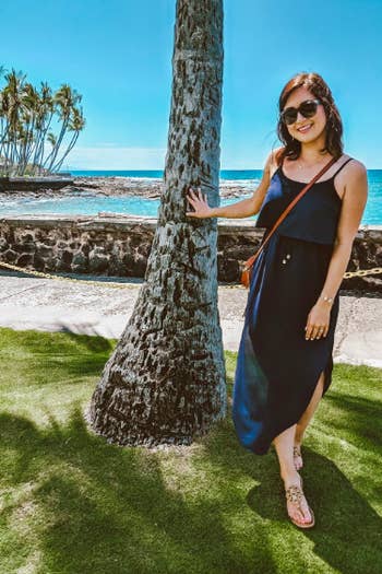 A reviewer wearing the spaghetti-strap dress with a rounded hem with slits at the sides in navy