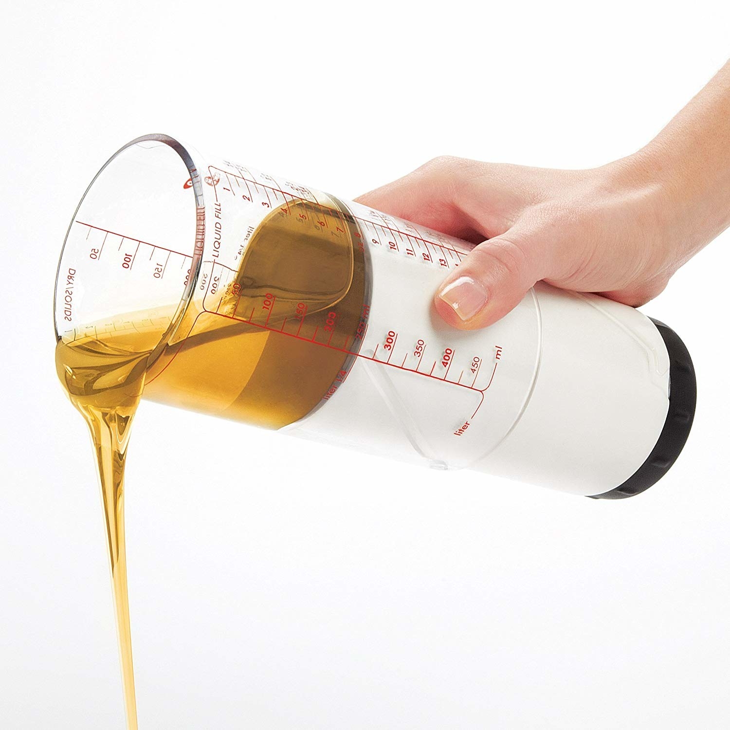 A hand pouring oil out of the cylindrical measuring cup, which features precise measurements etched on the side