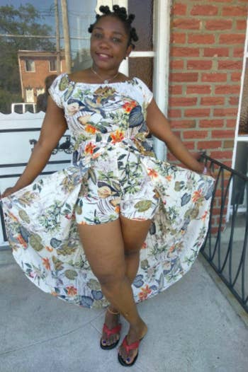 A reviewer wearing the dress in white with orange and green floral print, holding the sides up to reveal the shorts