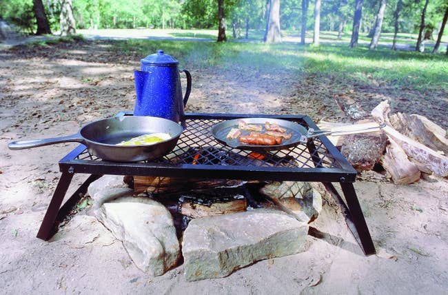 metal grate over campfire with two pans and a coffee percolator on top