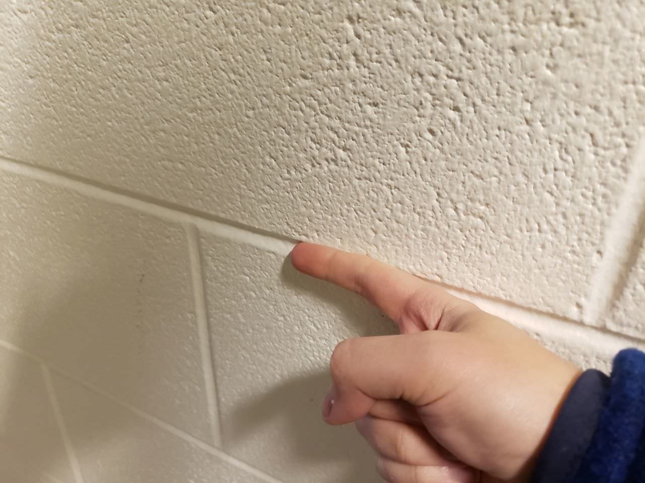 A hand with a pointing finger touches a textured brick wall, highlighting a narrow groove between bricks