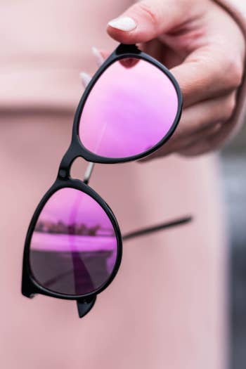 hand holding black-rimmed glasses with mirrored pink/purple lenses