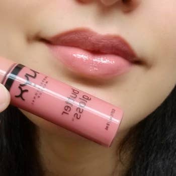 A reviewer wearing and holding up a tube of the light pink gloss