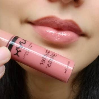 A reviewer holding a tube of the light pink shade up to their pink, glossy lips