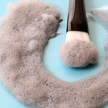 The gray foaming mask next to a brush