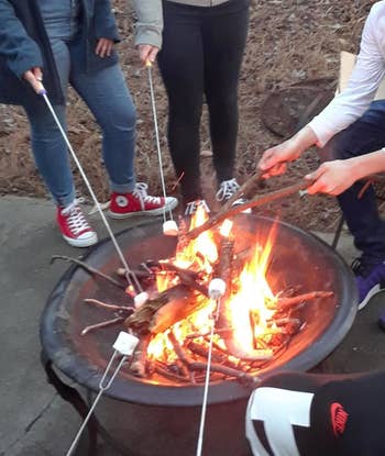 reviewers roasting marshmallows on the skewers over a fire