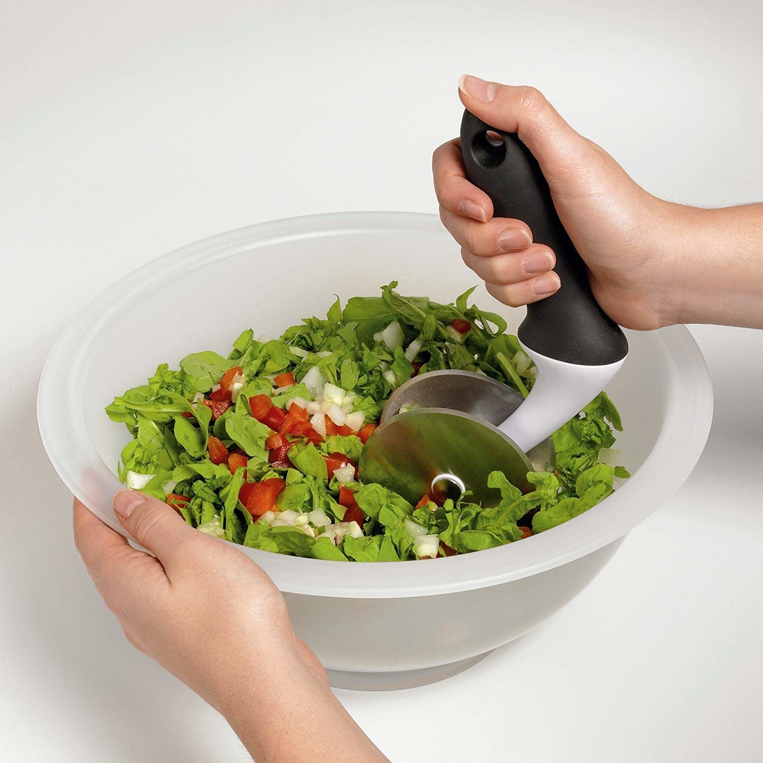 Hands rolling the double-pizza cutter-esque chopper through a bowl of greens and veggies