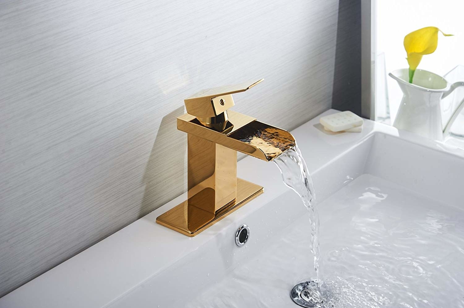 Gold waterfall faucet pouring out water into a sink