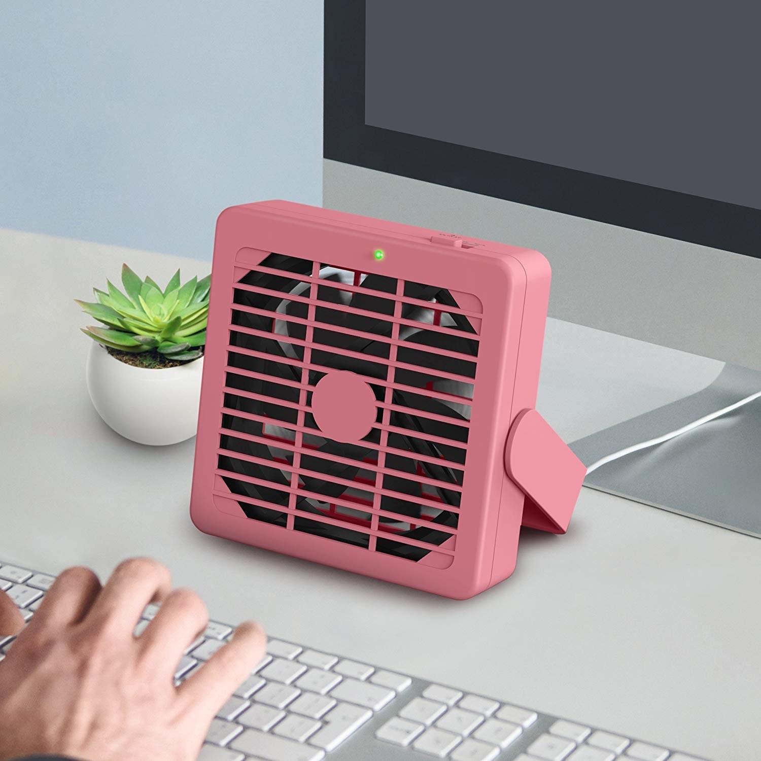 A small square-shaped pink fan on a desk 