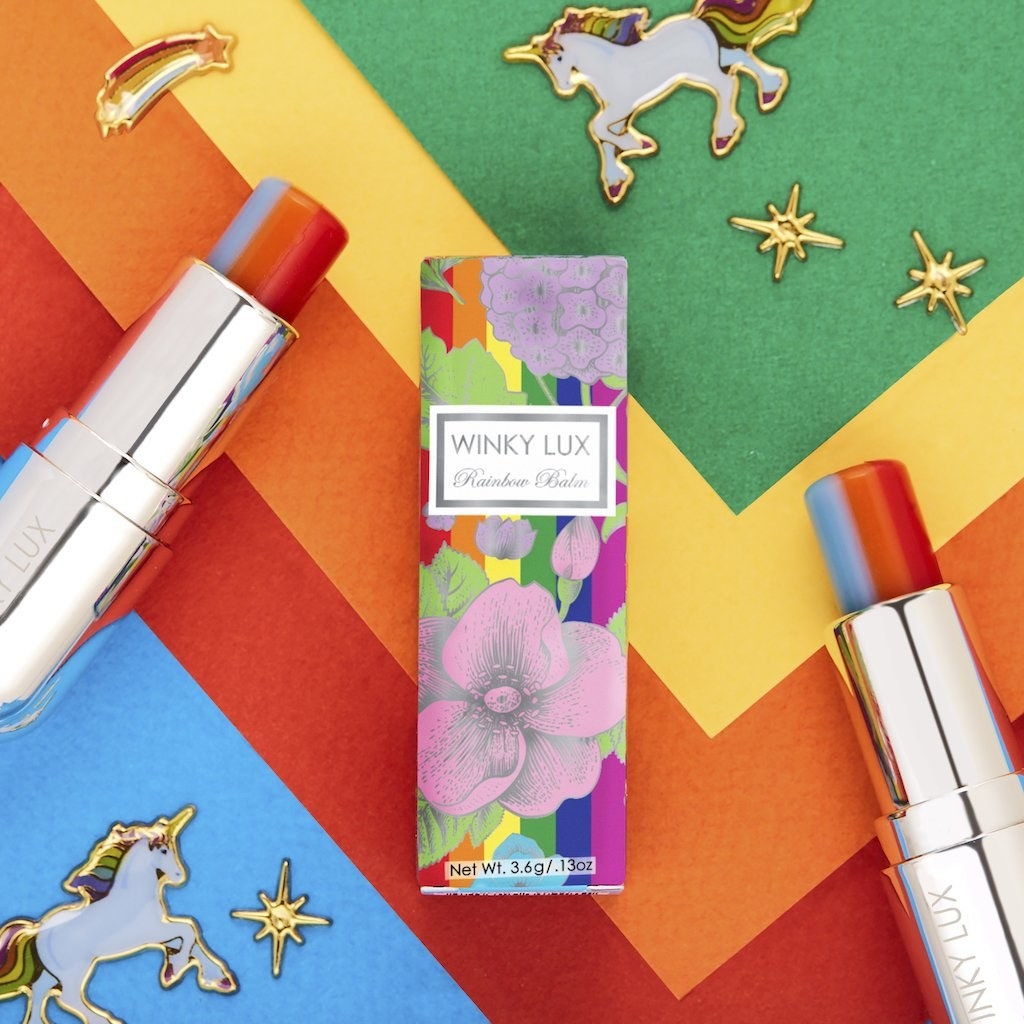 a lipstick tube in a floral rainbow colored box, the product is blue, orange, and red striped
