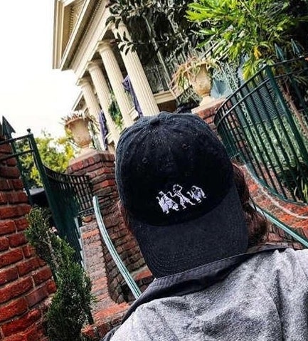 a model wearing a black hat on backwards with the hitchhiking ghosts embroidered on it 