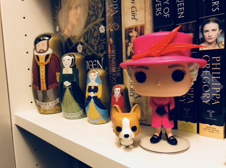 a reviewer photo of the queen elizabeth funko pop featuring a pink hat and outfit and a corgi companion