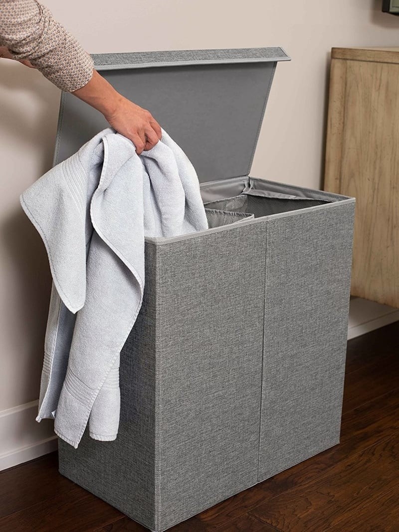 The laundry basket in grey with a model lifting the attached lid to put a towel into one of the two compartments