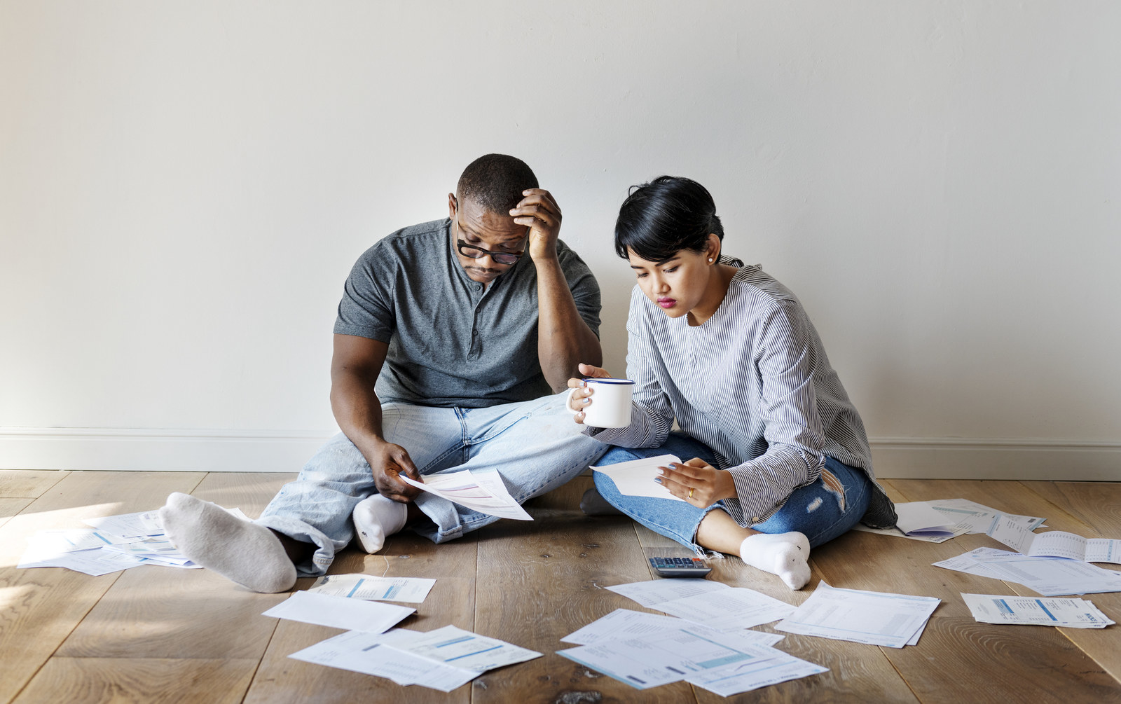 Confused-looking man and woman sitting on floor and sorting through papers
